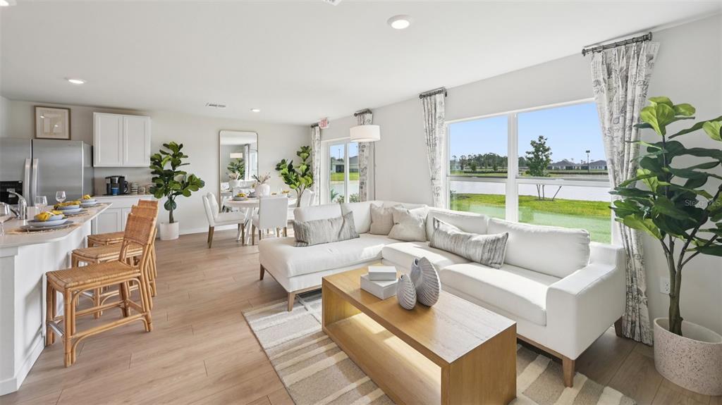 A bright open-concept living room and kitchen feature light wood floors, white furniture, and windows — 1554 POWELL VALLEY DRIVE, PORT CHARLOTTE, FL