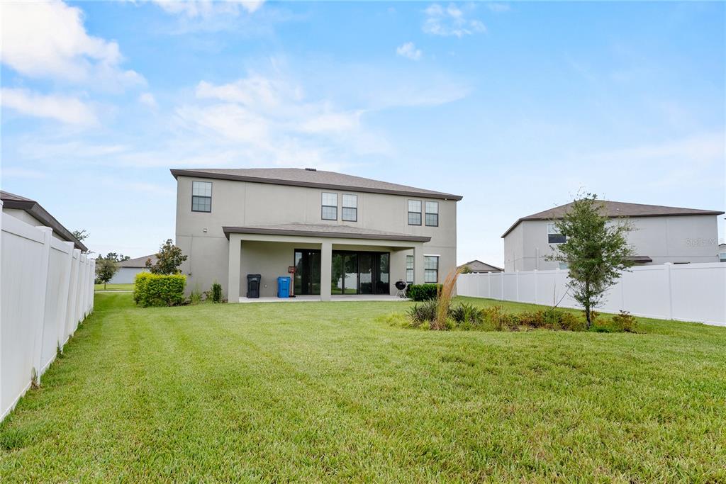 The backyard of a two-story house features a covered patio and a white vinyl fence — 12642 BERGSTROM BAY DRIVE, RIVERVIEW, FL