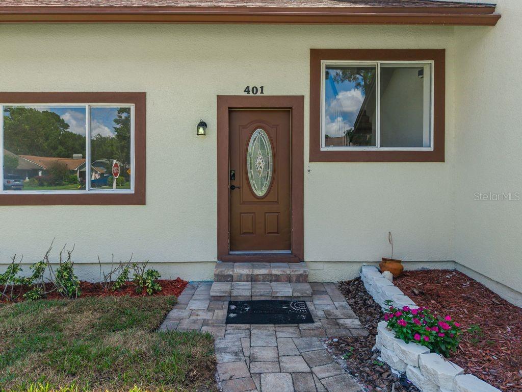 The exterior of a home features a brown front door, two windows, and a walkway — 401 WOODVIEW DRIVE, LONGWOOD, FL
