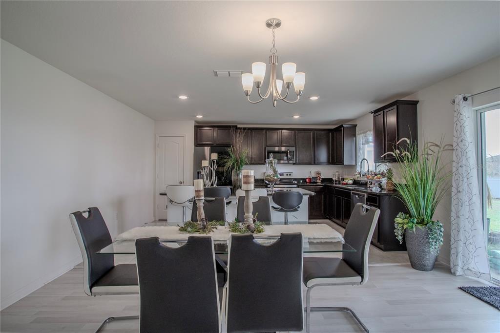 A dining area with a glass table and dark chairs opens to a modern kitchen — 605 SARNER PASS WAY, WINTER HAVEN, FL