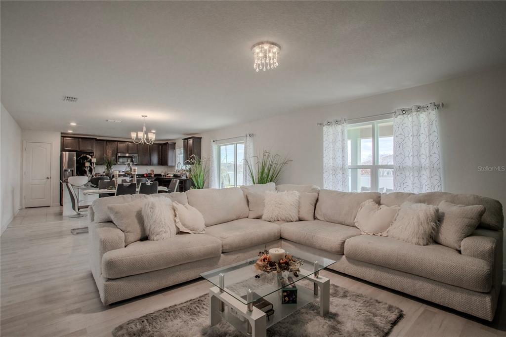 A living room with a large sectional sofa, glass coffee table, and an open-concept kitchen — 605 SARNER PASS WAY, WINTER HAVEN, FL