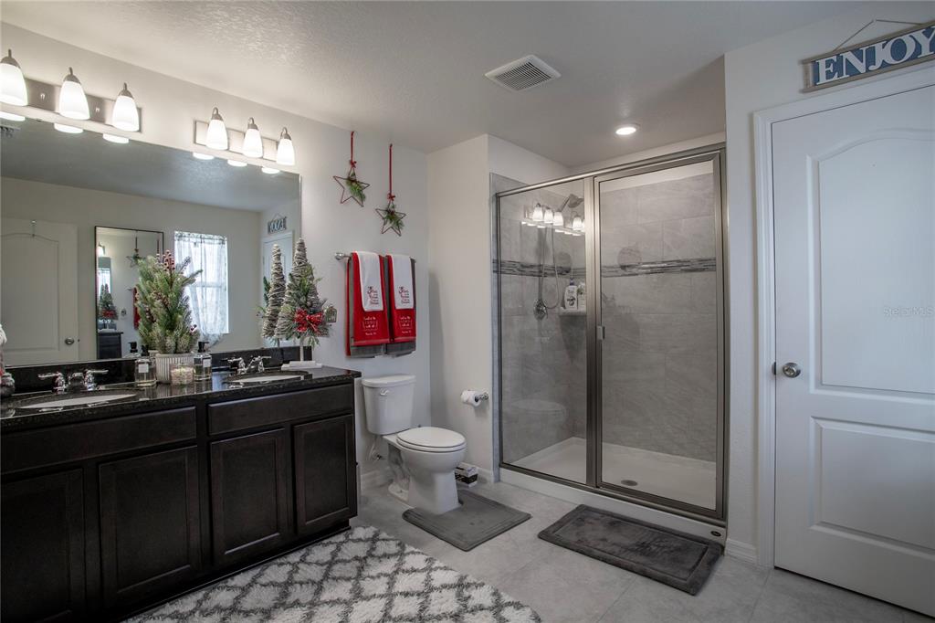 A bathroom features a dark wood double vanity, a glass-enclosed shower, and tiled flooring — 605 SARNER PASS WAY, WINTER HAVEN, FL