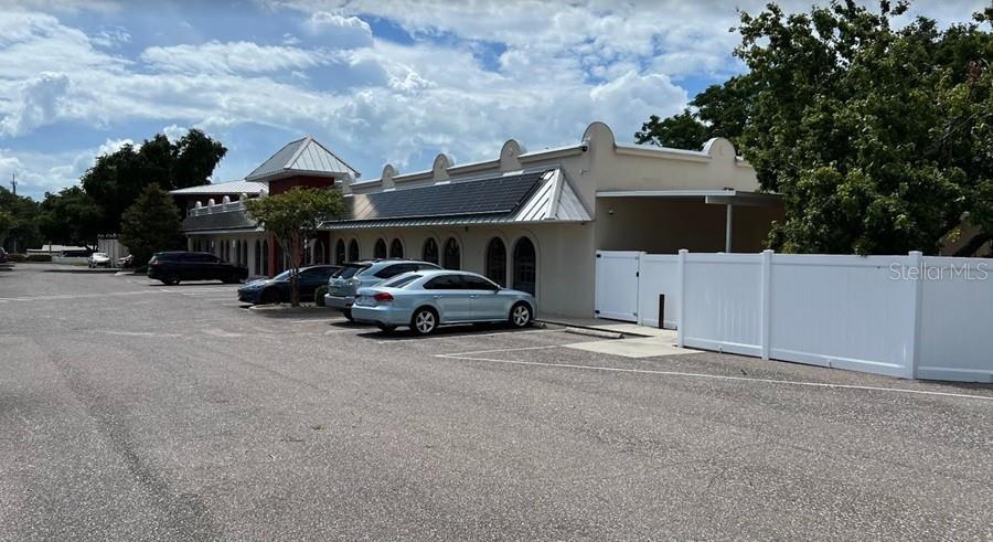 A light-colored commercial building with a metal roof and a white vinyl privacy fence — 1550 MAIN STREET, DUNEDIN, FL