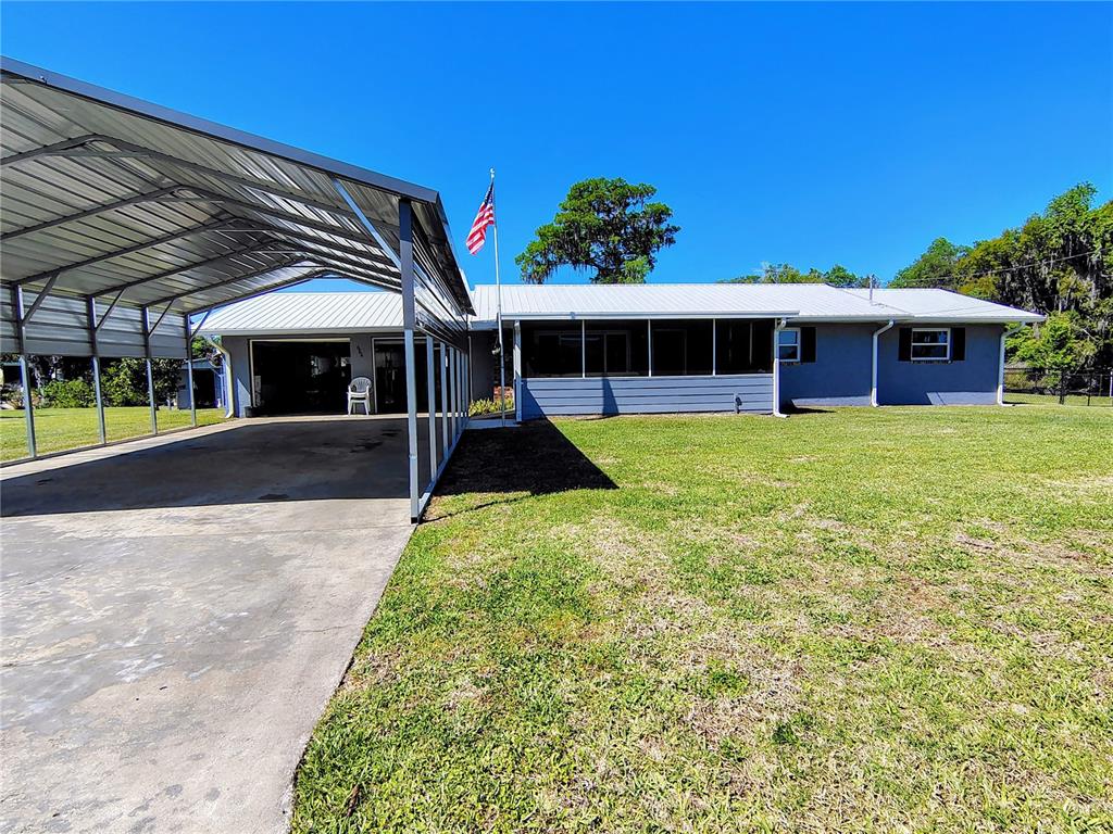 A gray house with a metal roof features a large attached carport and front lawn — 664 CR 467, LAKE PANASOFFKEE, FL