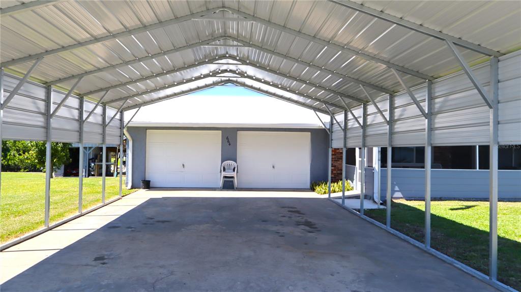 A metal carport stands in front of a house with two white garage doors — 664 CR 467, LAKE PANASOFFKEE, FL
