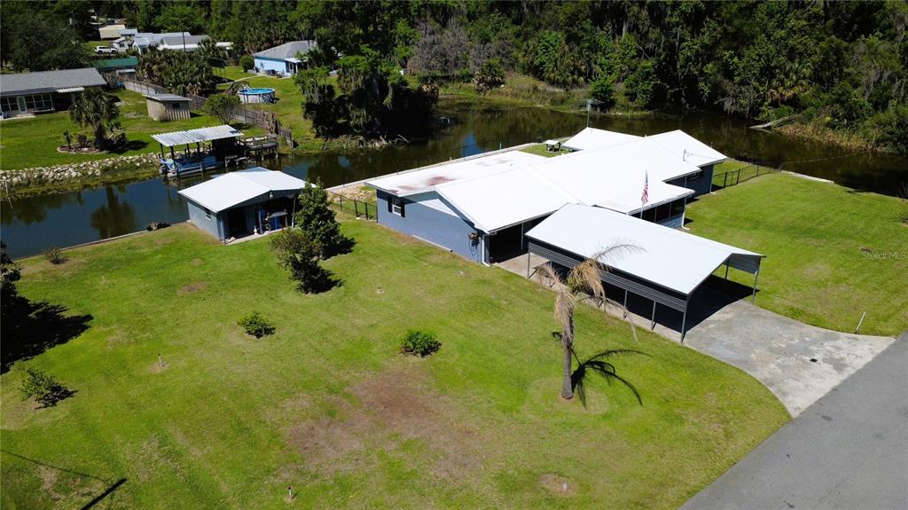 An aerial view shows a house with a metal roof, carport, and detached garage by water — 664 CR 467, LAKE PANASOFFKEE, FL