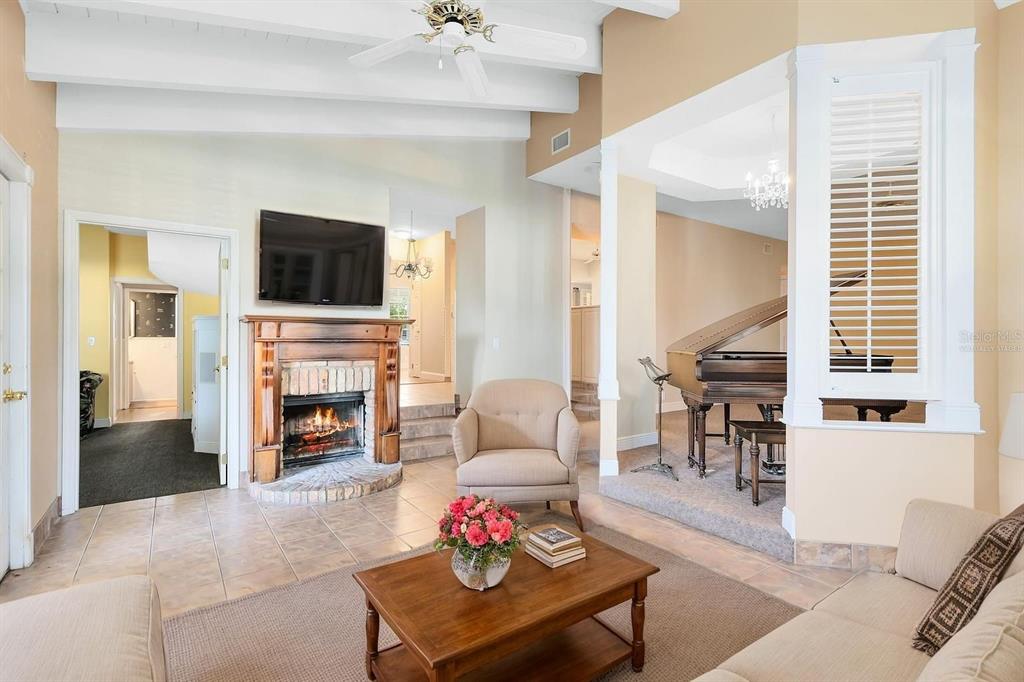 A living room features a fireplace, a grand piano on a raised platform, and tile flooring — 910 CYPRESS AVENUE, ST CLOUD, FL