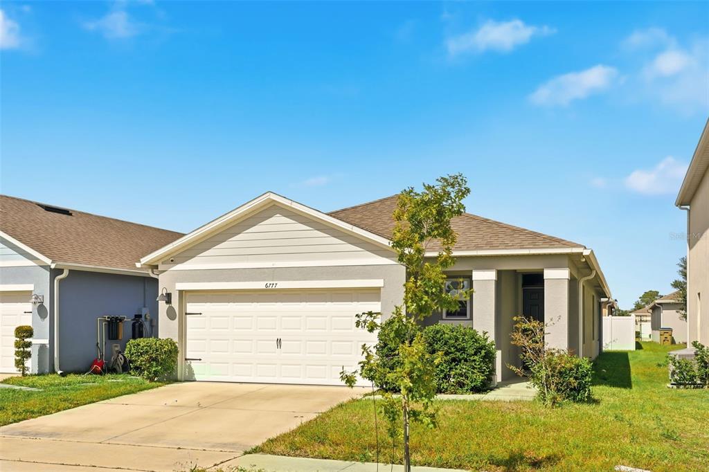 A single-story suburban house with a two-car garage and a light-colored stucco exterior — 6777 HUNTLEIGH HAMMOCK ROAD, HARMONY, FL