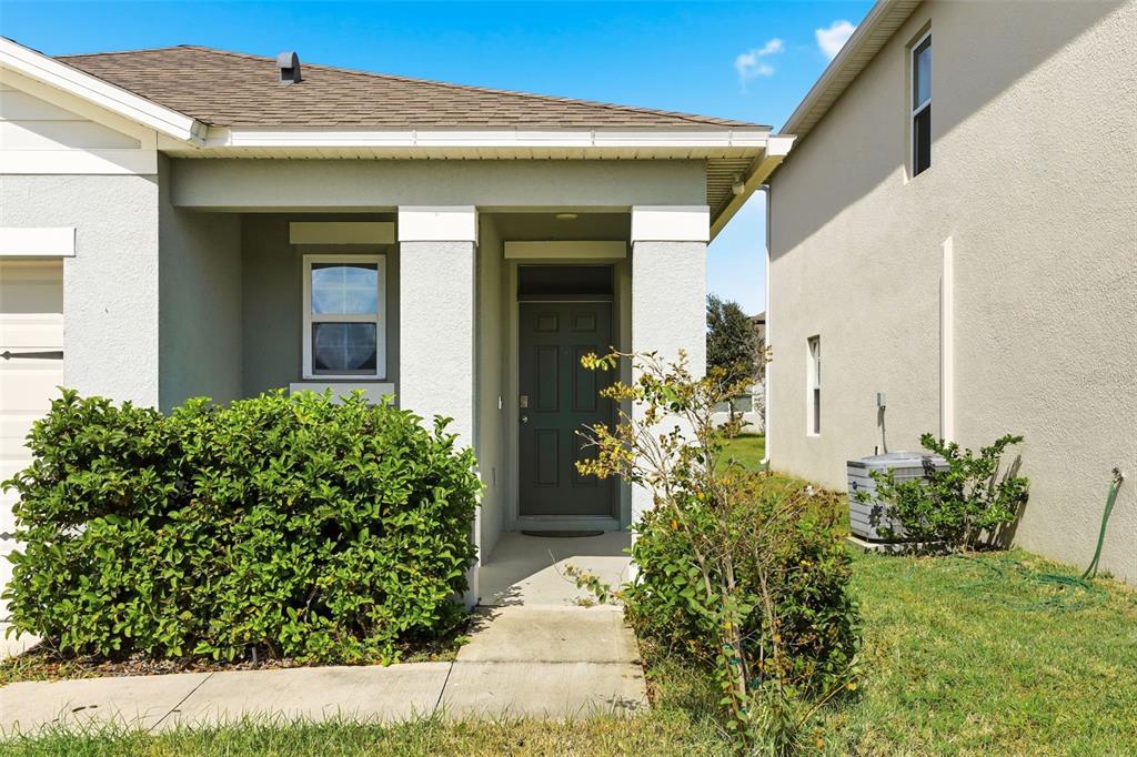 The exterior of a house features a covered entryway, a dark front door, and landscaping — 6777 HUNTLEIGH HAMMOCK ROAD, HARMONY, FL
