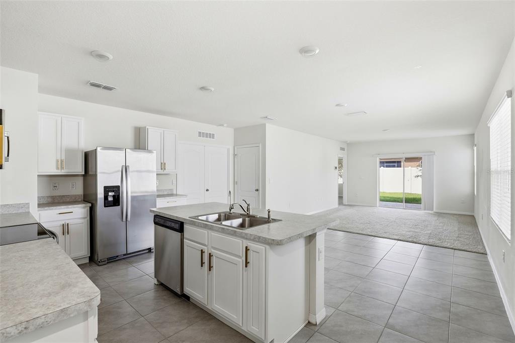 A kitchen with white cabinets and stainless steel appliances opens to a carpeted living area — 6777 HUNTLEIGH HAMMOCK ROAD, HARMONY, FL