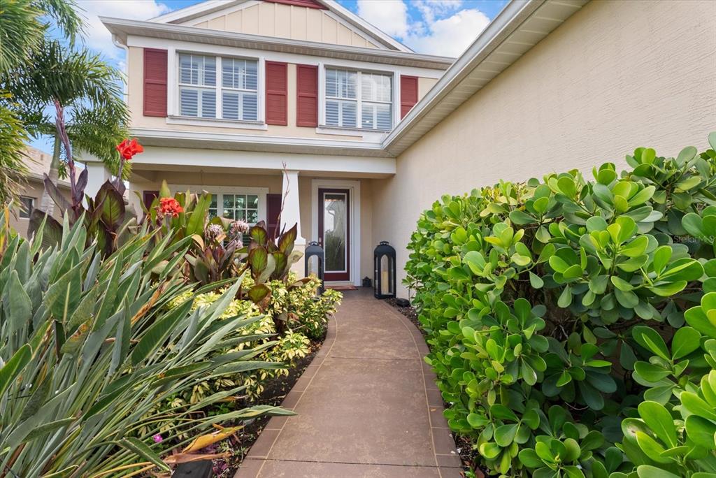 A concrete walkway leads to the front entrance of a two-story home with red shutters — 4522 CEDAR BRUSH TERRACE, SARASOTA, FL