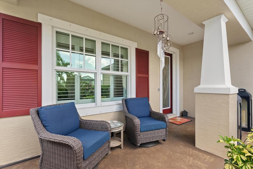 A covered front porch features two wicker chairs with blue cushions and red window shutters — 4522 CEDAR BRUSH TERRACE, SARASOTA, FL