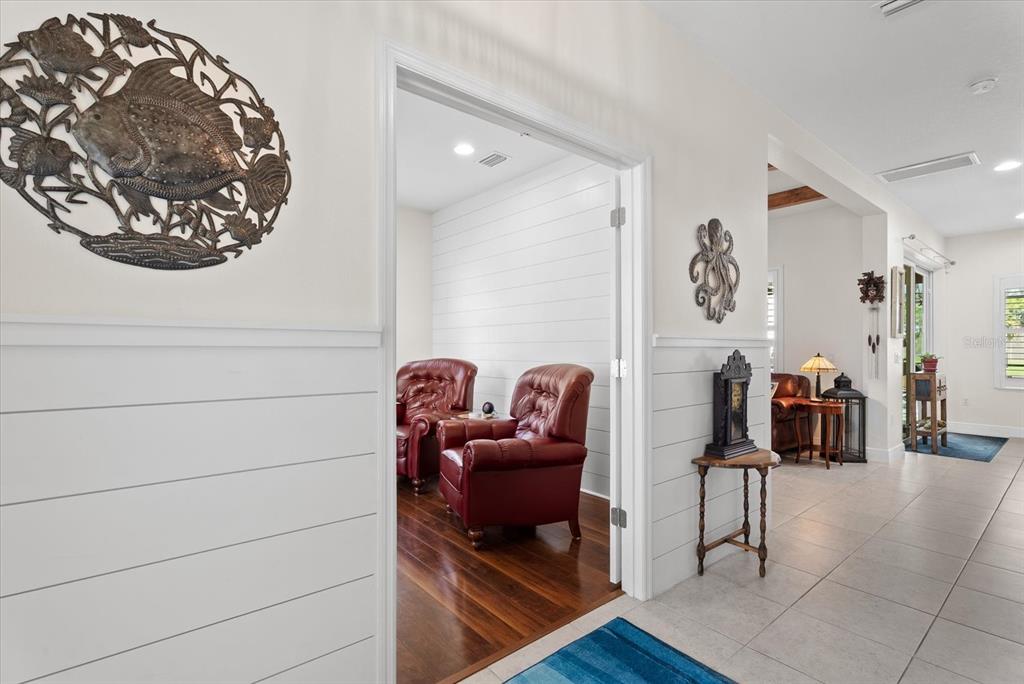 A hallway with white shiplap walls leads into a room featuring two red leather chairs — 4522 CEDAR BRUSH TERRACE, SARASOTA, FL