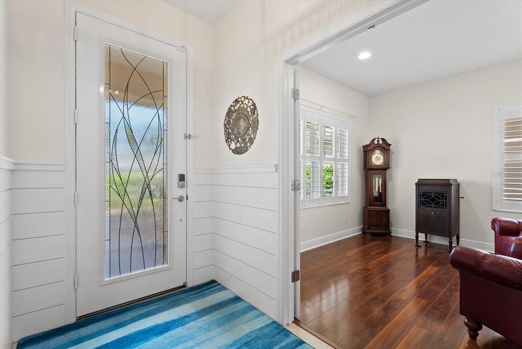 An entryway with white shiplap walls and a glass-paneled door leads into a wood-floored room — 4522 CEDAR BRUSH TERRACE, SARASOTA, FL