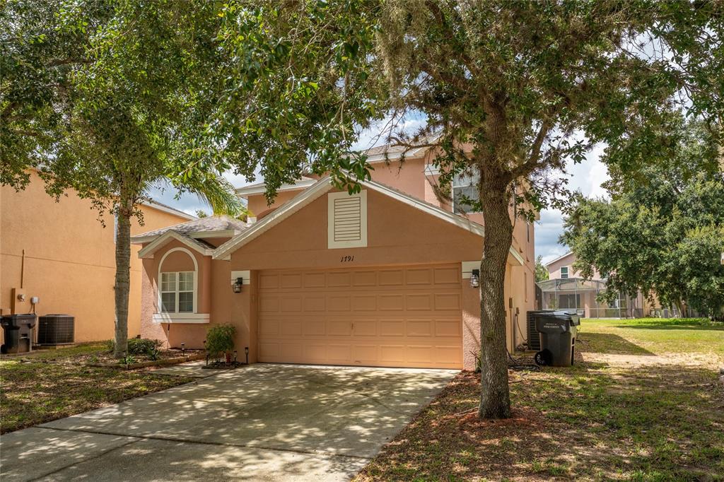 A two-story peach-colored house features a two-car garage and a concrete driveway — 1791 ROYAL RIDGE DRIVE, DAVENPORT, FL