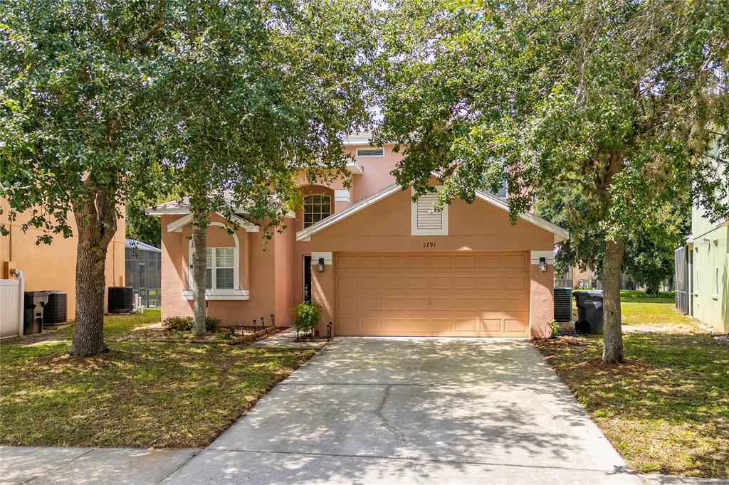 A two-story peach-colored house features a two-car garage and a concrete driveway — 1791 ROYAL RIDGE DRIVE, DAVENPORT, FL