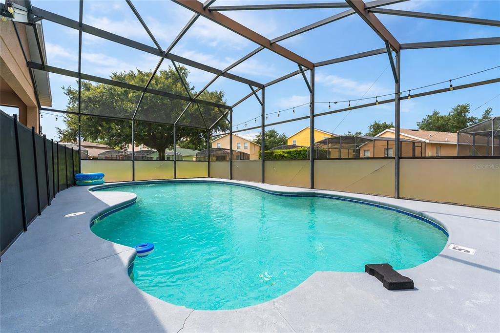 A swimming pool with a screen enclosure sits on a gray concrete patio — 1791 ROYAL RIDGE DRIVE, DAVENPORT, FL
