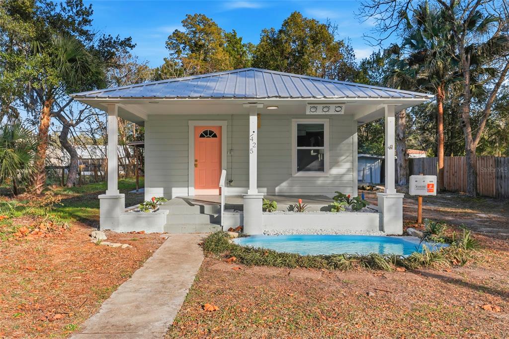 A light green cottage with a metal roof, coral front door, and a small front pond — 425 SE 2ND STREET, WILLISTON, FL