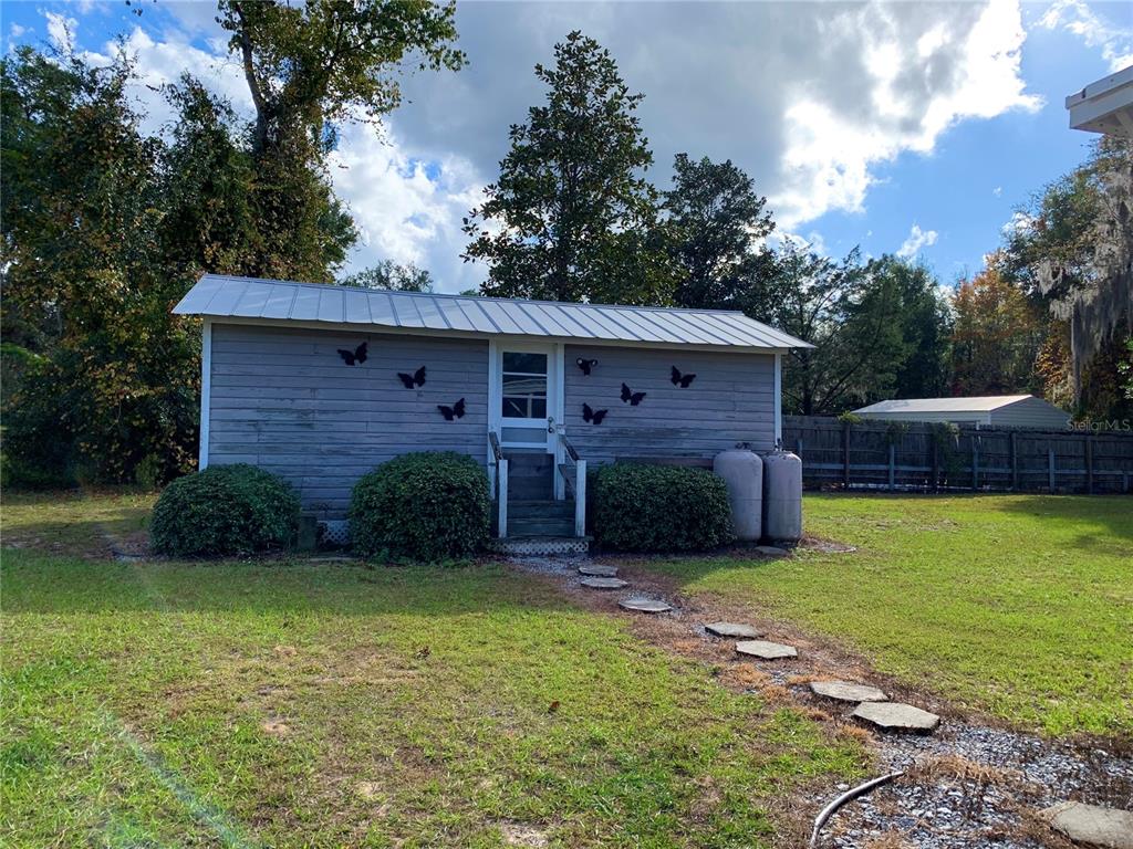 A small, gray, single-story shed with a metal roof sits in a grassy yard — 17630 NE 246TH PLACE, FORT MC COY, FL