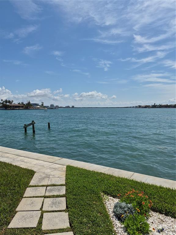 A stone walkway leads through a grassy lawn toward a waterfront view with wooden pilings — 1505 PASS A GRILLE WAY UNIT 31, ST PETE BEACH, FL
