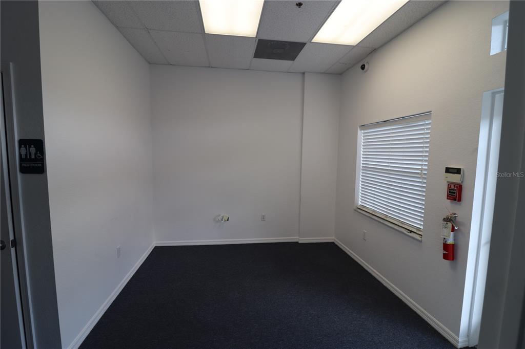 An empty office with white walls, dark carpet, a window with blinds, and a fire extinguisher — 144 TRIPLE DIAMOND BOULEVARD UNIT F, NOKOMIS, FL