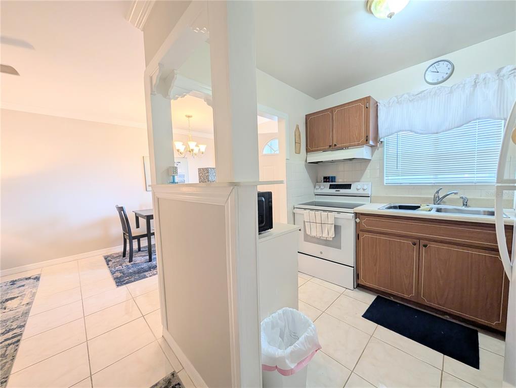 A kitchen with wood cabinets and white appliances opens to a dining area with tile — 1839 SUNNY DRIVE UNIT E36, BRADENTON, FL