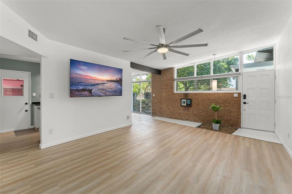 A living room features light wood flooring, a brick accent wall, and a ceiling fan — 7712 HOOSIER PLACE, ORLANDO, FL