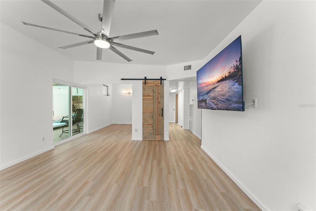 A living room features light wood-look flooring, a ceiling fan, and a sliding barn door — 7712 HOOSIER PLACE, ORLANDO, FL