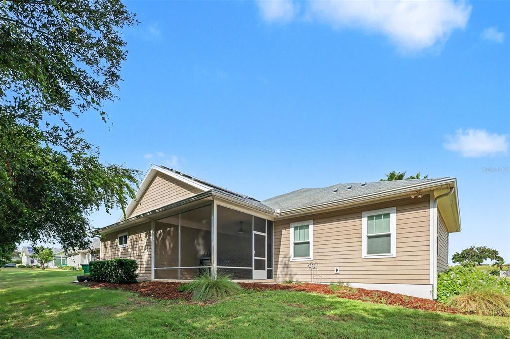The exterior of a tan, single-story house features a screened-in porch and a grassy yard — 1182 FIESTA KEY CIRCLE, LADY LAKE, FL