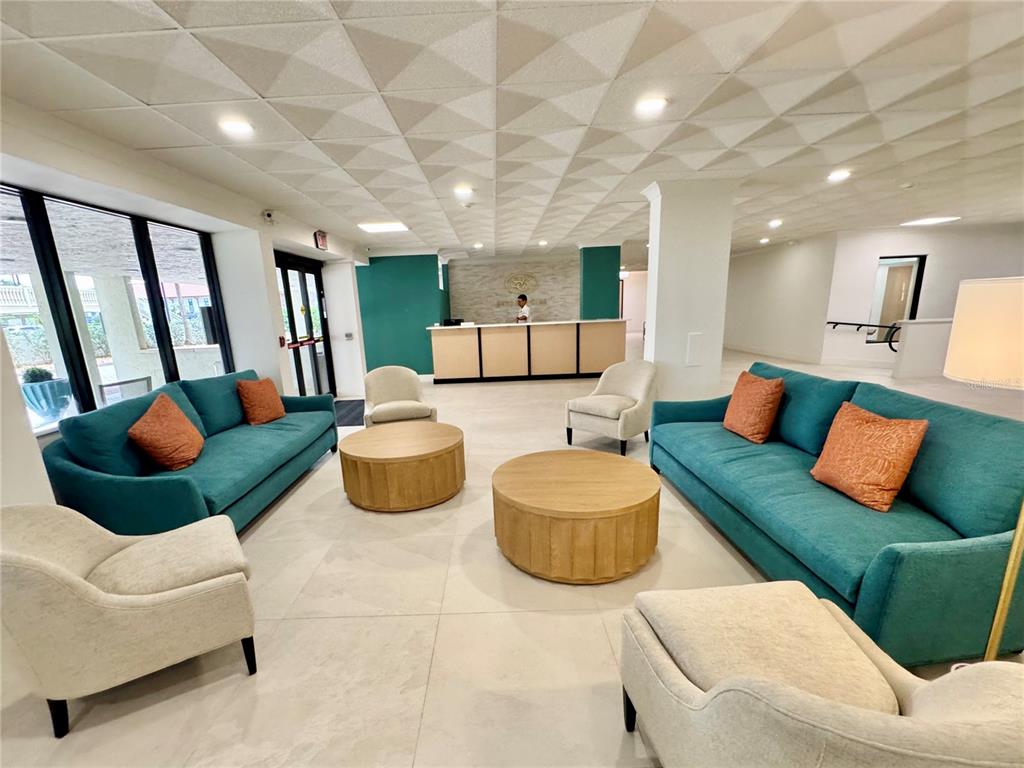 A lobby features teal sofas, light-colored armchairs, round wooden coffee tables, and a reception desk — 1380 GULF BOULEVARD UNIT 805, CLEARWATER, FL