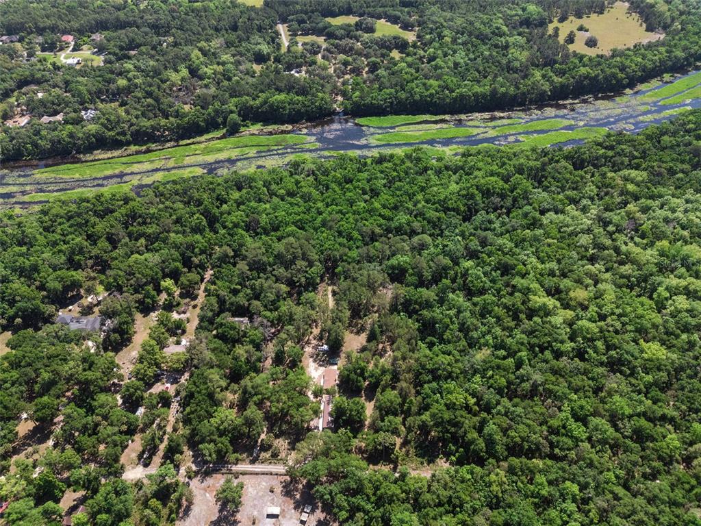 An aerial view shows a house nestled in a dense forest beside a winding river — BRONSON ROAD, SORRENTO, FL