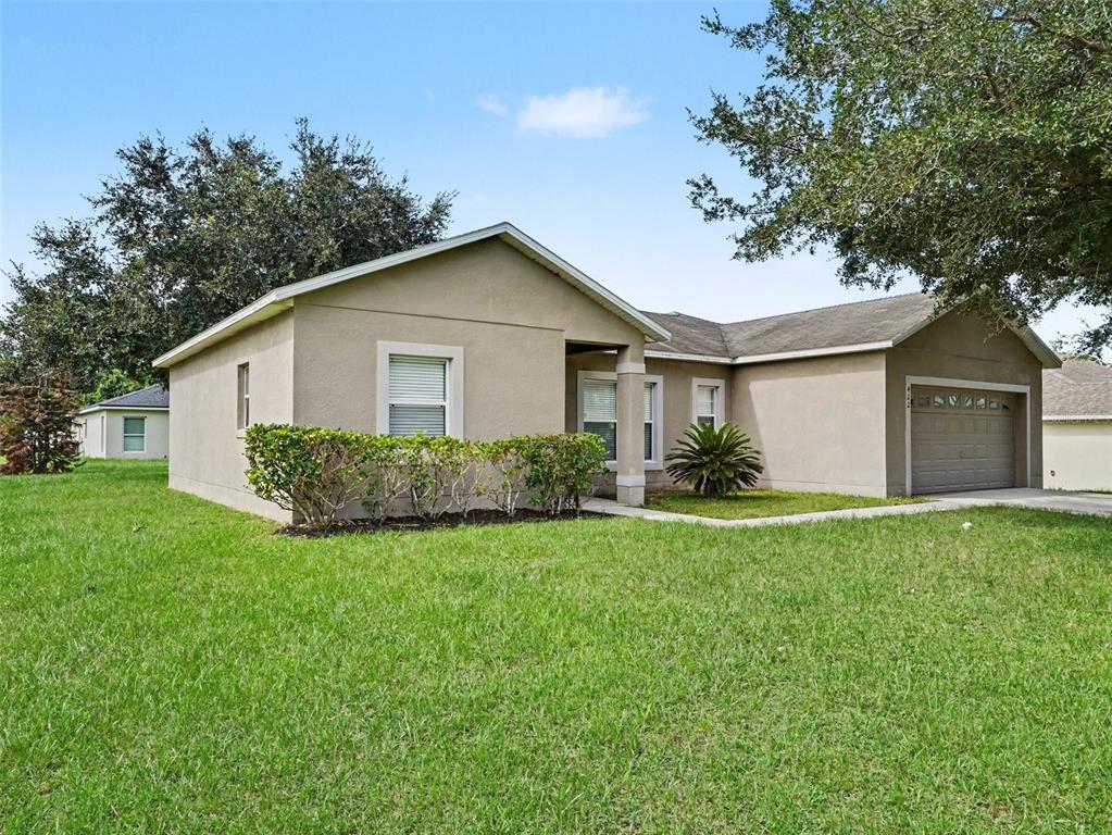 A single-story tan stucco house features a front-facing garage and a manicured lawn — 422 COLUMBIA COURT, POINCIANA, FL
