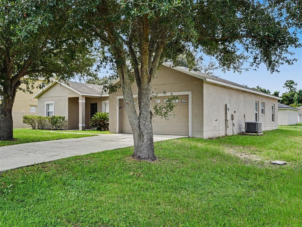 A single-story house with a beige stucco exterior, a two-car garage, and a large tree — 422 COLUMBIA COURT, POINCIANA, FL