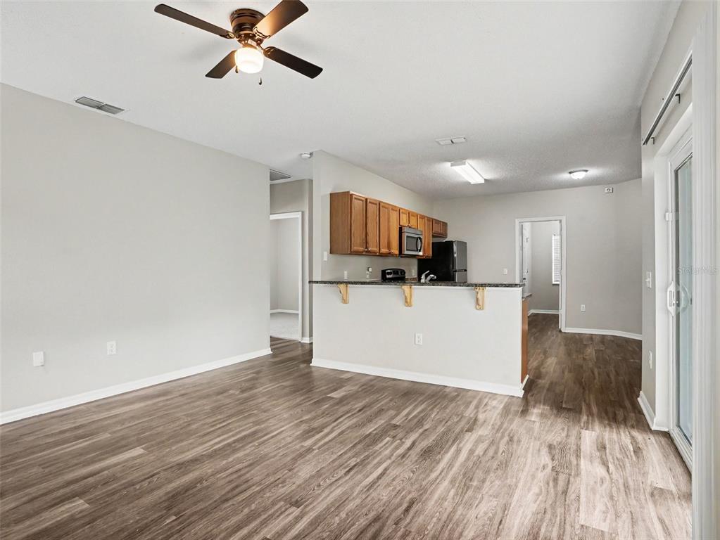 An open-concept living area features wood-look flooring, a ceiling fan, and a kitchen with cabinets — 422 COLUMBIA COURT, POINCIANA, FL
