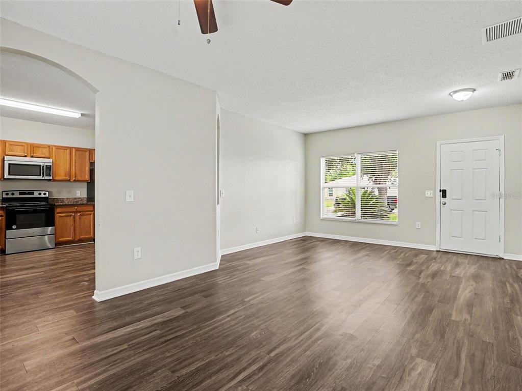 A living room with wood-look flooring, light gray walls, and an adjacent kitchen with cabinets — 422 COLUMBIA COURT, POINCIANA, FL