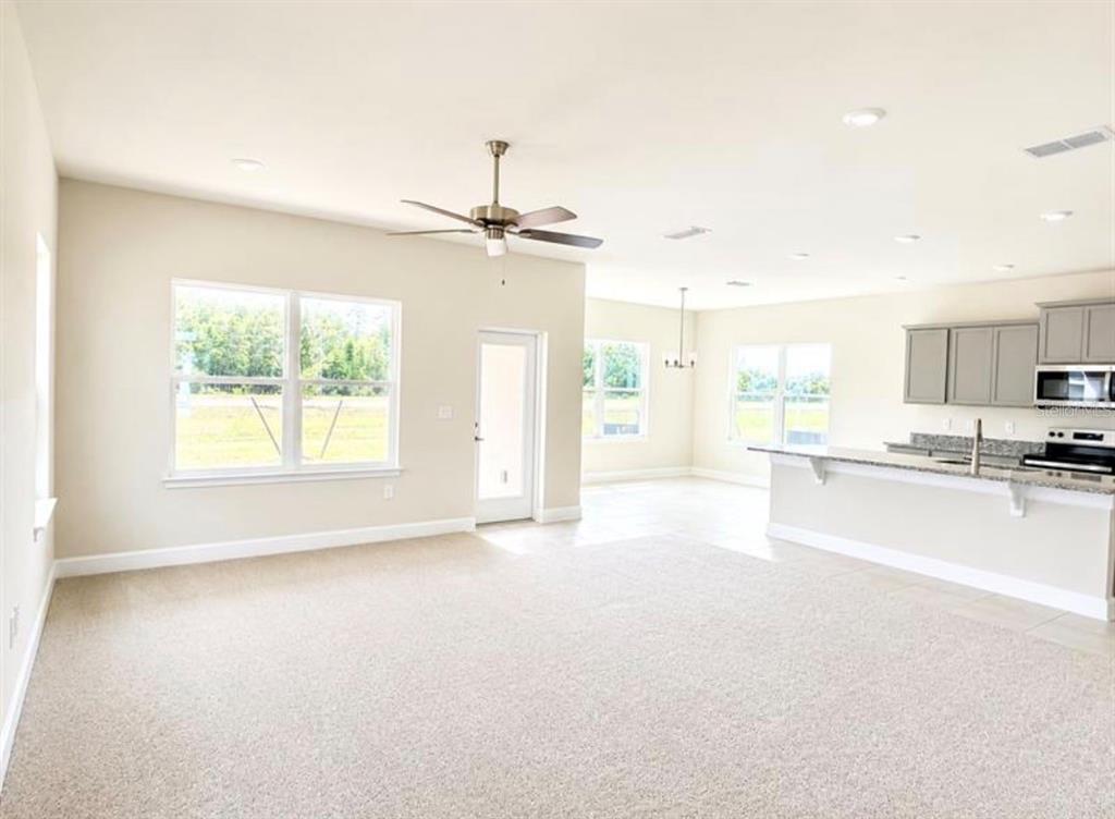 A spacious room with gray carpeting, white walls, a ceiling fan, and three windows — 7727 BENT TREE LOOP, ST CLOUD, FL