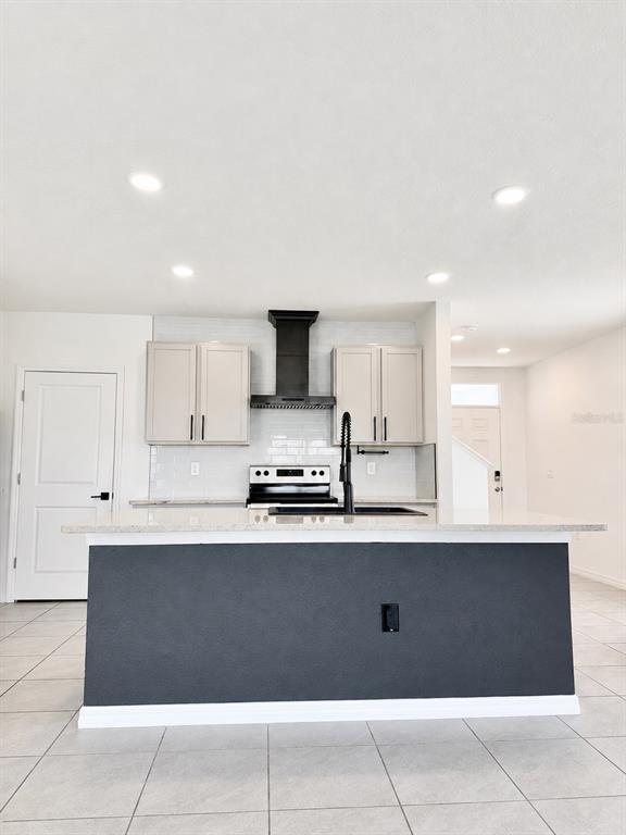 A kitchen features a dark island, light cabinets, a black range hood, and tile flooring — 34110 JASPER STONE DRIVE, WESLEY CHAPEL, FL