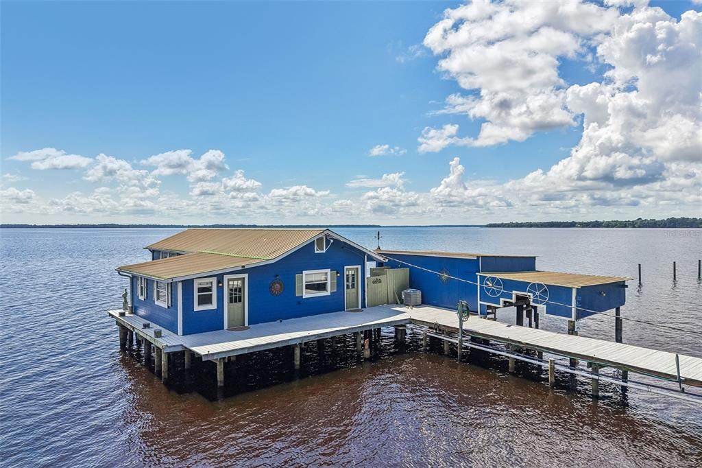 A blue house on stilts sits over the water with a wooden deck and walkway — 21 S LAKE STREET, CRESCENT CITY, FL