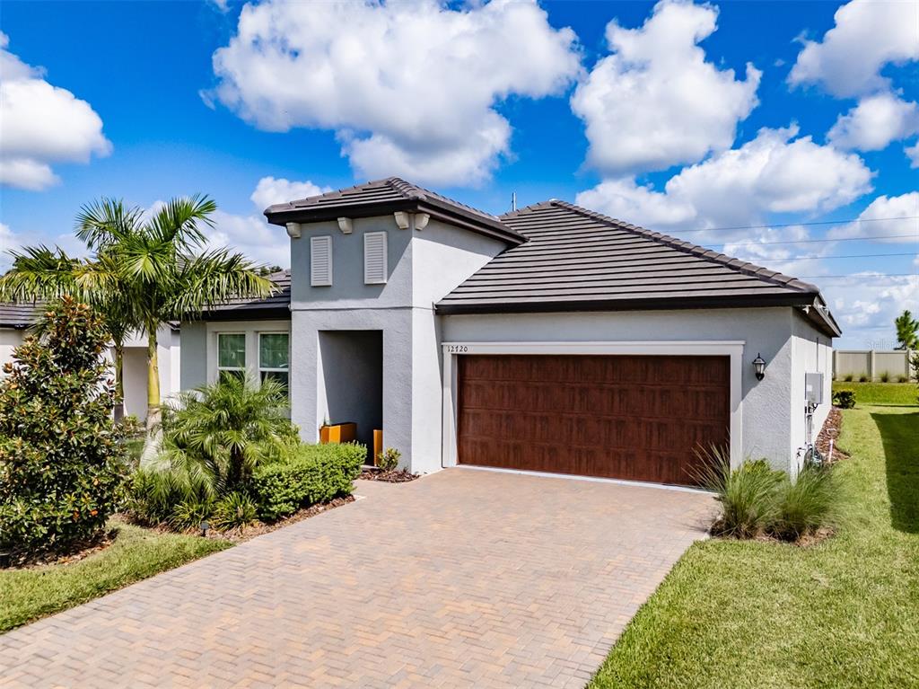 A single-story house with a gray stucco exterior, a brown tiled roof, and a paved driveway — 12720 TAHITIAN PEARL, PARRISH, FL