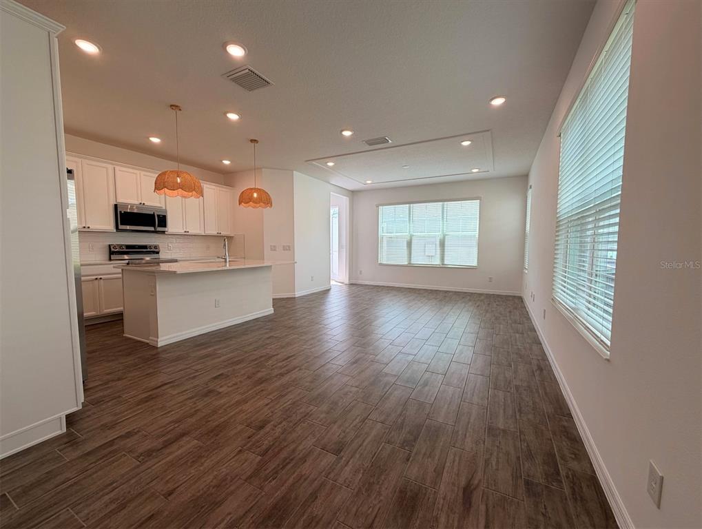 An open-concept kitchen and living area featuring white cabinetry, a kitchen island, and wood-look flooring — 7036 BOLANZO ALLEY, WINTER GARDEN, FL
