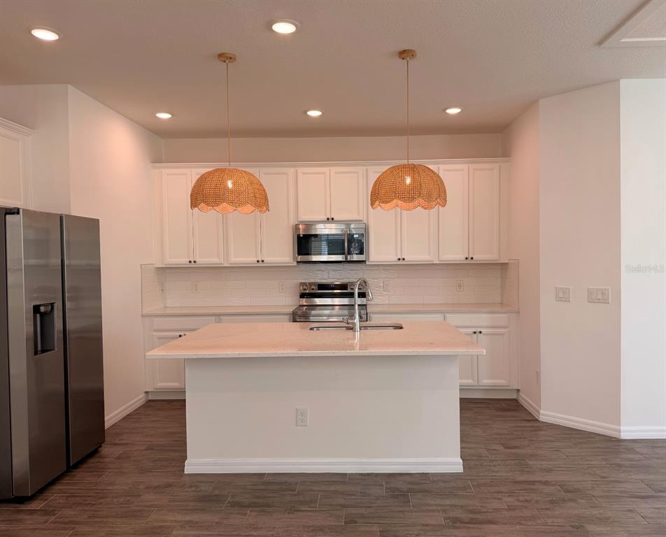 A kitchen with white cabinets, stainless steel appliances, a center island, and two woven pendant lights — 7036 BOLANZO ALLEY, WINTER GARDEN, FL