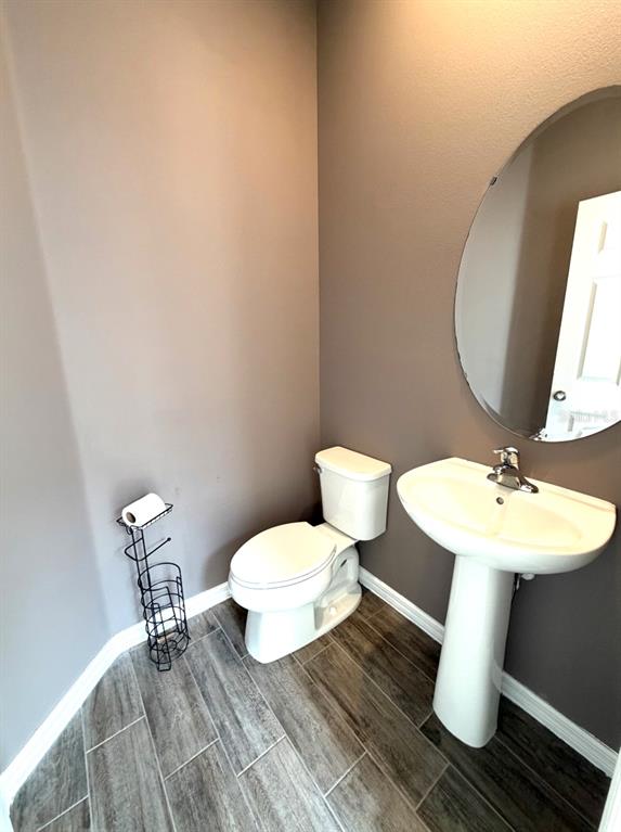 A half bathroom features a pedestal sink, an oval mirror, a toilet, and wood-look tile flooring — 7036 BOLANZO ALLEY, WINTER GARDEN, FL