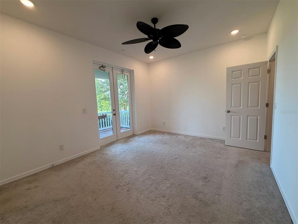 An empty bedroom features beige carpeting, white walls, a ceiling fan, and glass doors to a balcony — 7036 BOLANZO ALLEY, WINTER GARDEN, FL