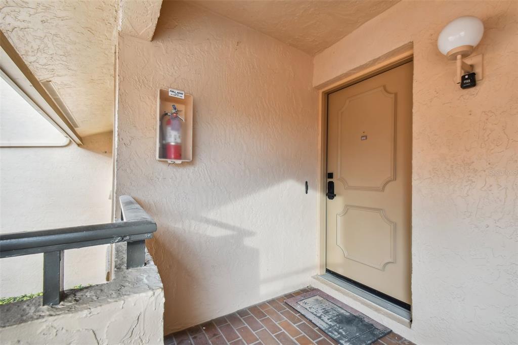 An exterior entryway features a tan door, a wall-mounted fire extinguisher, and a brick floor — 4800 BRITTANY DRIVE S UNIT 102, ST PETERSBURG, FL