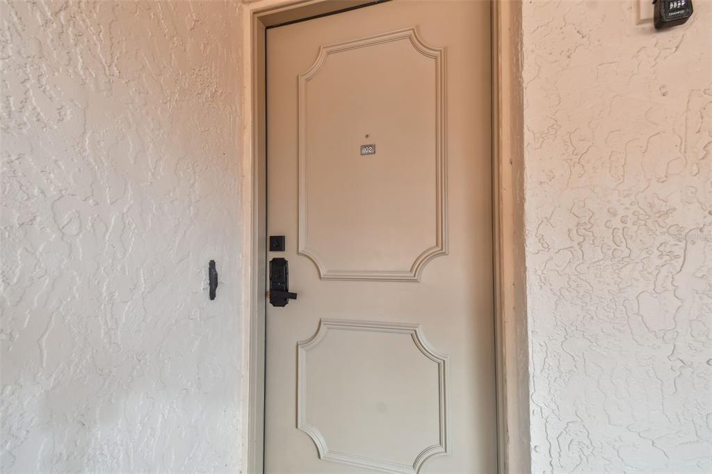 A beige door with a number 102 plaque is set into a textured white wall — 4800 BRITTANY DRIVE S UNIT 102, ST PETERSBURG, FL