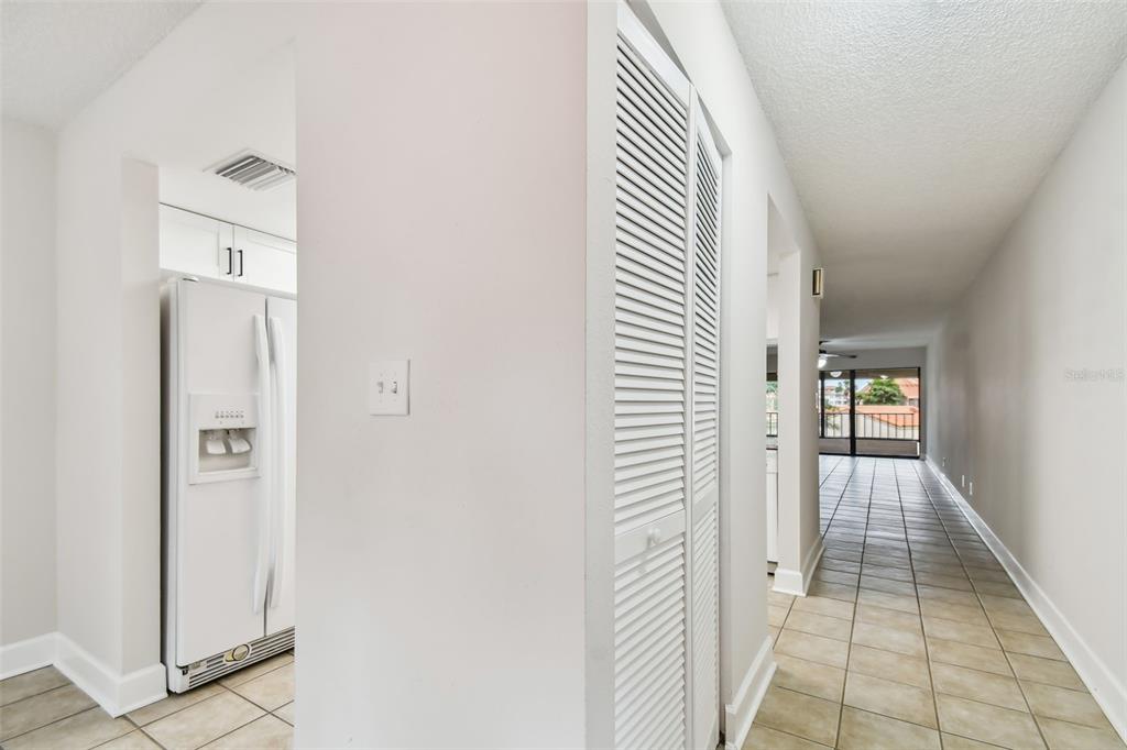 A hallway with tiled floors leads past a louvered closet toward a bright living area — 4800 BRITTANY DRIVE S UNIT 102, ST PETERSBURG, FL