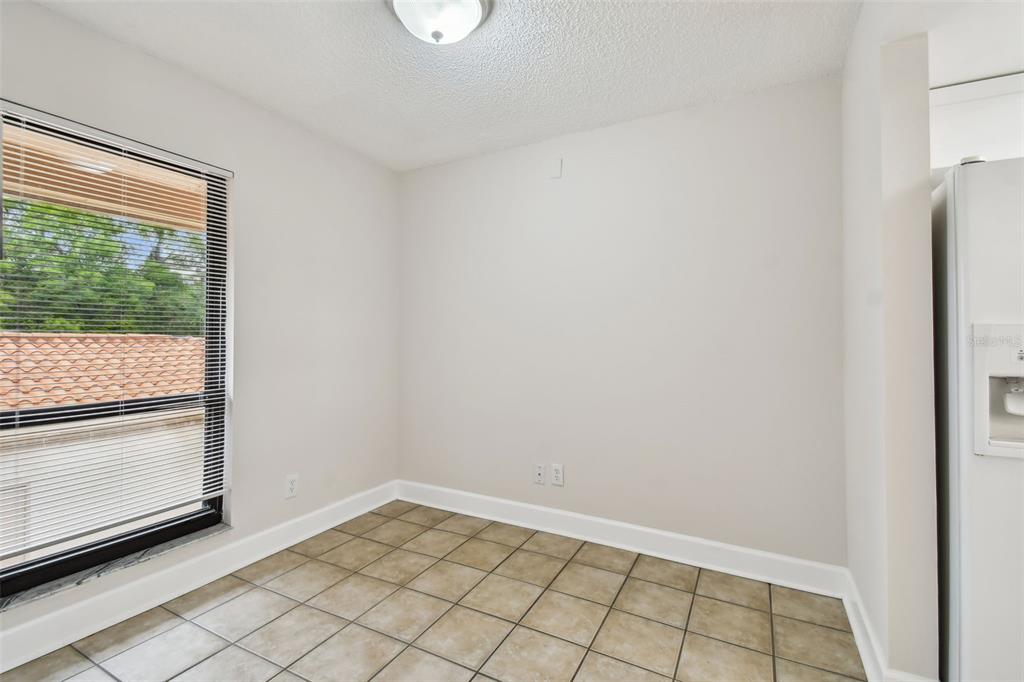 A small, empty dining area with beige tile flooring, white walls, and a large window — 4800 BRITTANY DRIVE S UNIT 102, ST PETERSBURG, FL
