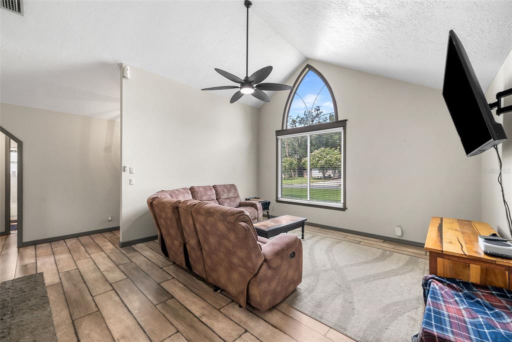 A living room features vaulted ceilings, a large arched window, wood-look tile flooring, and a sofa — 9 TEAK COURT, OCALA, FL
