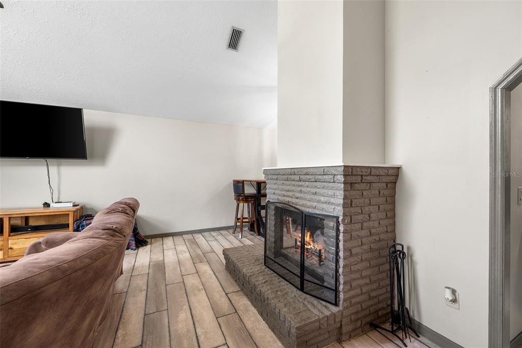 A living room features a gray brick fireplace, wood-look tile flooring, and a wall-mounted television — 9 TEAK COURT, OCALA, FL