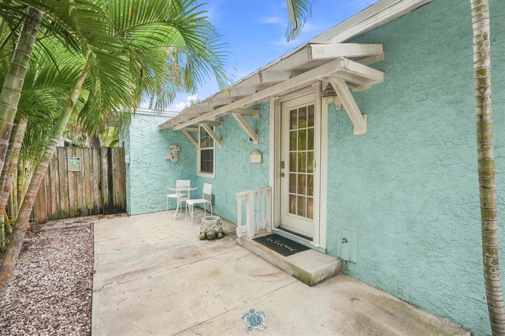 A light blue stucco house exterior features a concrete patio, a glass-paneled door, and palm trees — 13123 4TH STREET E, MADEIRA BEACH, FL